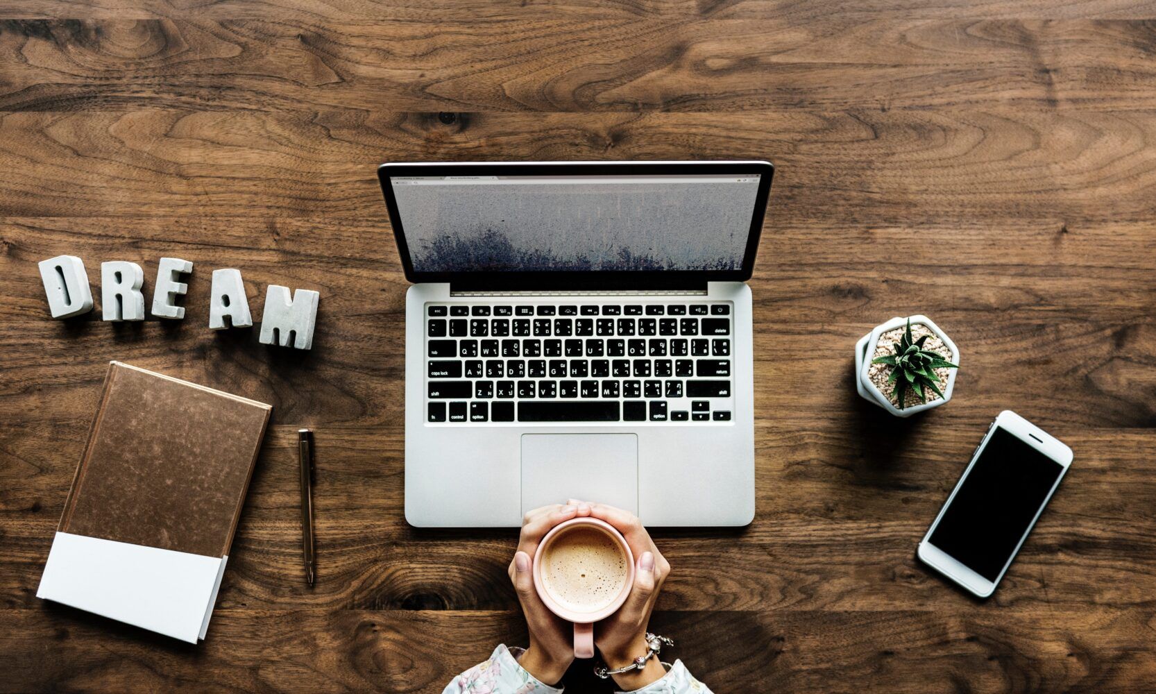 Image of an open laptop and hands holding a cup of coffee, and the person is getting ready to write a review of an eating disorder treatment center. The word Dream spelled out next to the computer.